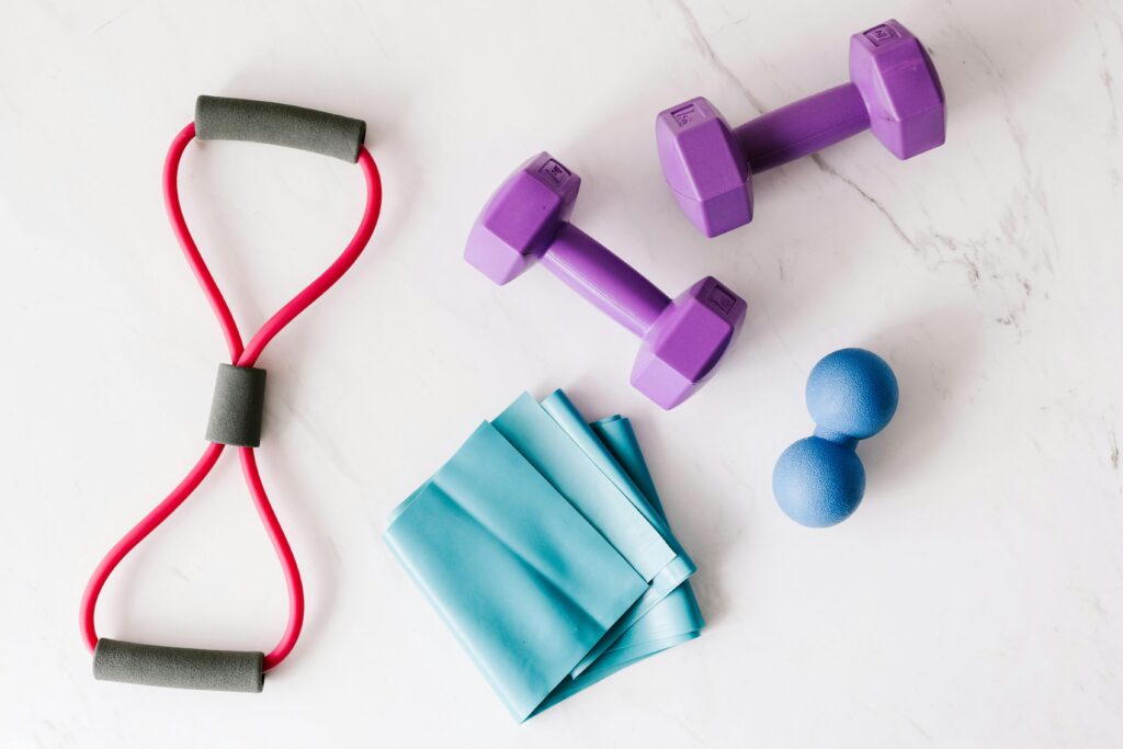 Top view of purple metal dumbbells and red tubular expander and blue tape expander and blue massage double ball placed on marble surface